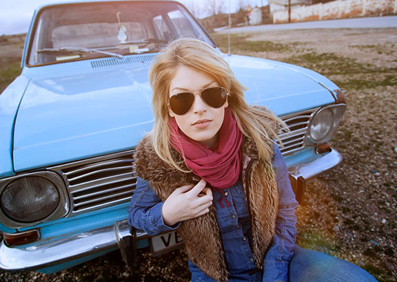 Frau sitzt auf einer Motorhaub und blickt in die Kamera